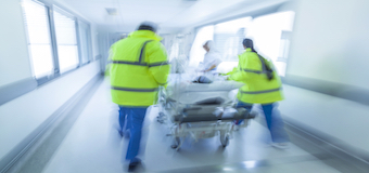 médicos e paramédicos empurrando maca com paciente num corredor hospitalar