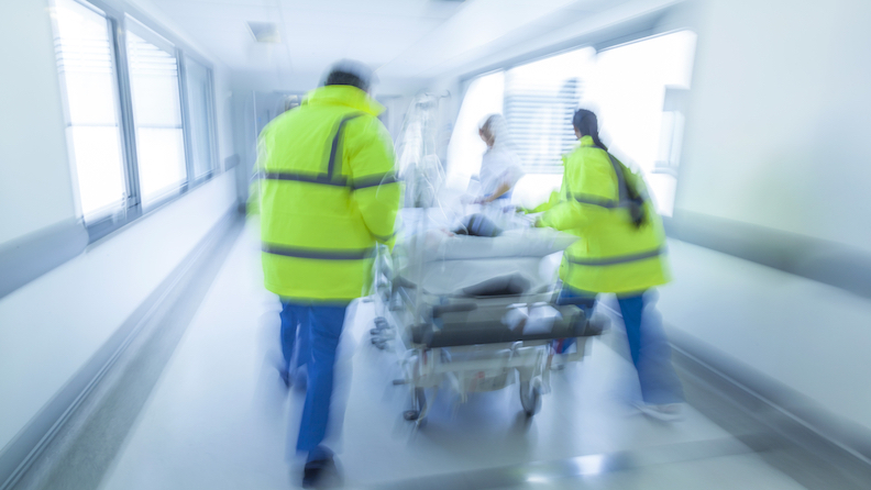 médicos e paramédicos empurrando maca com paciente num corredor hospitalar
